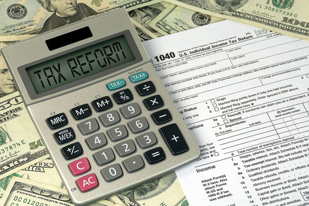 calculator and a form 1040 on a pile of money with tax reform on the calculator